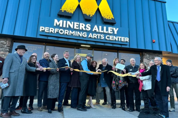 A group of people cutting the ribbon in front of Miners Alley Performing Arts Center