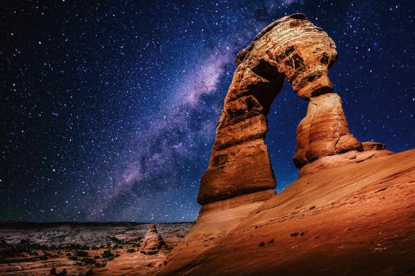 Delicate Arch framed by the Milky Way stretching across the night sky in Arches National Park.