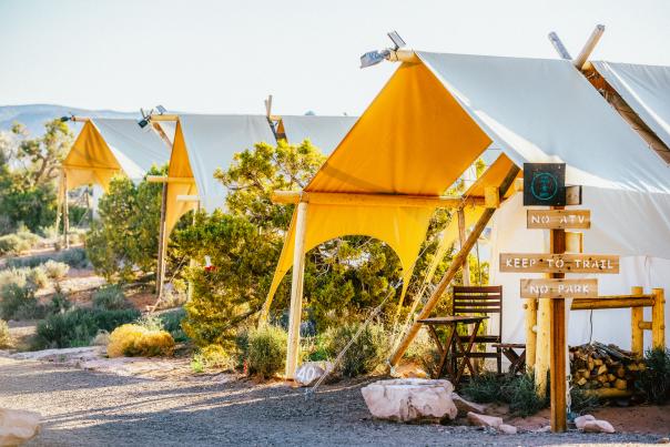 Safari-style canvas tents at Under Canvas Moab surrounded by desert vegetation under a bright blue sky.