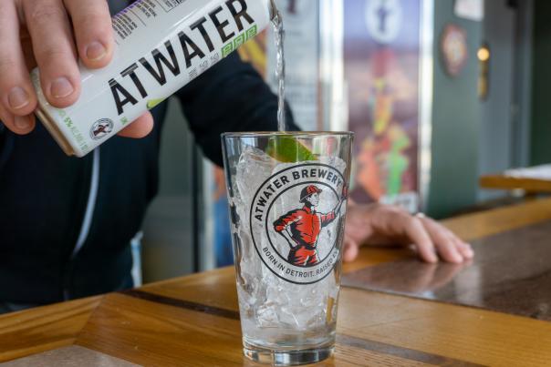Pouring hard seltzer from a can into an Atwater Brewery branded pint glass.