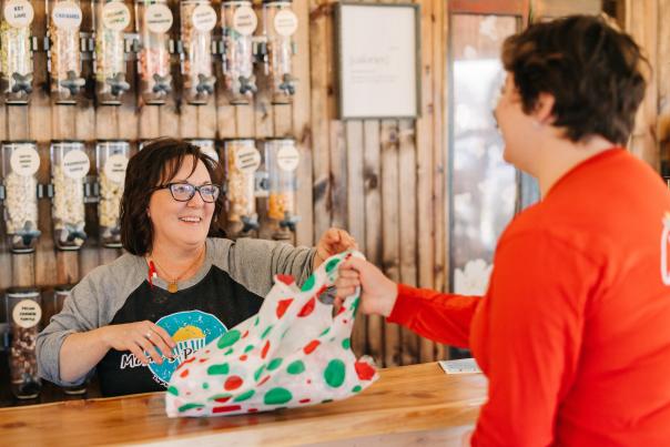 Cashier handing customer their purchase in a holiday bag at Mom's Popcorn