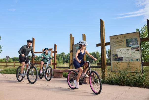 Family Biking outdoors on the Poudre River Trail with sign behind them