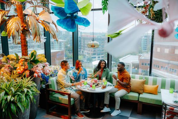 Group of four adults enjoying cocktails and food at Juniper, a uniquely decorated rooftop restaurant overlooking Downtown Greenville, SC.