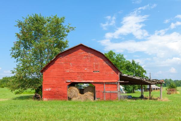 A Southern red barn filled with hay bales with a bright blue sky as a backdrop in Landrum, SC.