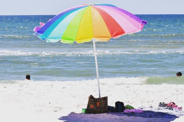 a rainbow colored umbrella on a sunny beach