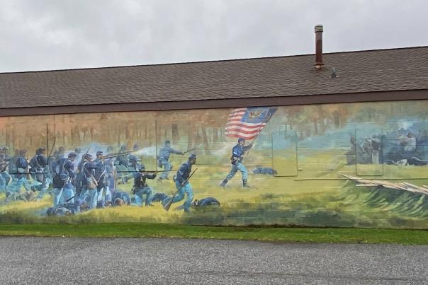 Painted mural of a civil war battle with African American soldiers on side of long building with brown roof