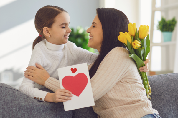 A mother and daughter holding a card with a heart and yellow flowers.