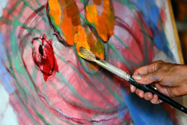 A hand applying paint to a canvas with a paintbrush.