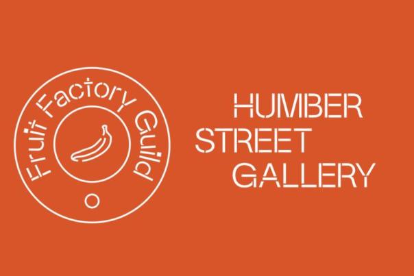 The Fruit Factory Guild logo from Humber street gallery. An orange background with white outlined writing. The drawing of a banana is in the centre of a circle and the words Fruit Factory Guild are above it within another circle.