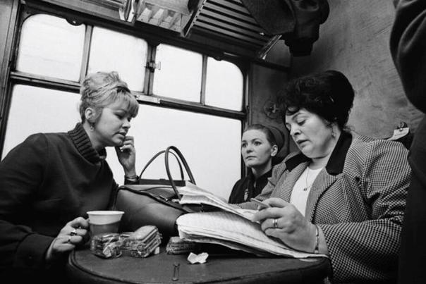 Lillian Bilocca, Yvonne Blenkinsop, Mary Denness and Christine Jensen MBE sit together at a small table in what appears to be a train compartment; one woman drinks from a paper cup, another looks ahead, and the third is reading or writing in a large notebook.
