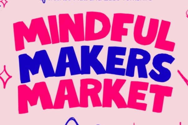 A light pink background with the words 'Mindful Makers Market' in cartoon style writing. Mindful and Market are in deep pink. Makers is in a bright blue colour. There are cartoon style outlines of safety pins and craft equipment around the sides.