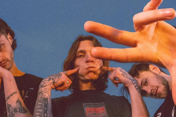 An image of band 'Mouth Culture'. 3 men stand together pulling faces at the camera in front of a blue background.