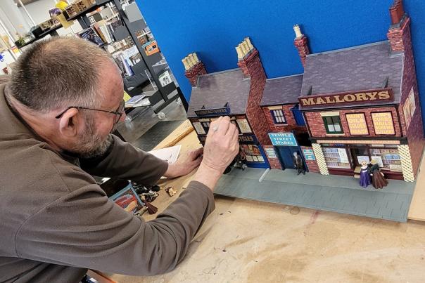 A man leans over a model of houses with a brush