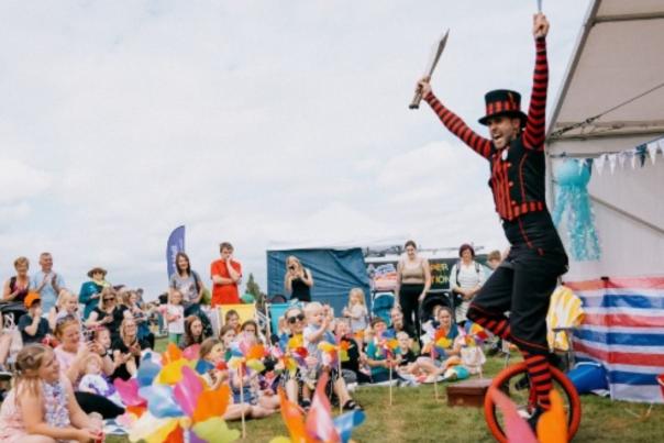 A man on a unicycle holds up swords to a crowd of people in a field