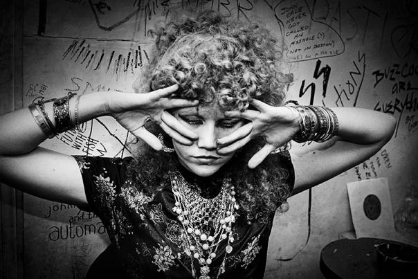 black and white photograph of a woman adorned with jewelry and peering through fingers