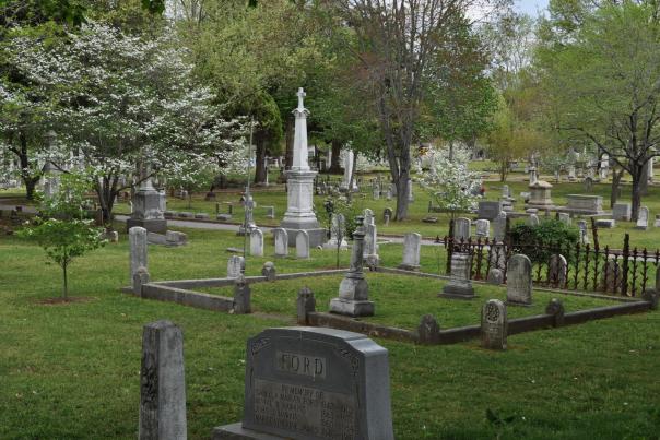 Historic gravestones and monuments surrounded by flowering trees and greenery at Maple Hill Cemetery in Huntsville, Alabama.