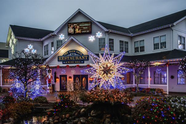 The Blue Gate Restaurant & Music Hall in Shipshewana at dusk, trimmed in Christmas lights, with a giant glowing star out front and lit shrubs around a rock garden.