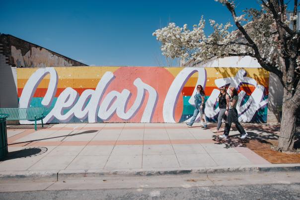 Brightly colored mural saying "Cedar City" with three women walking and blossoms on the trees framing either side.