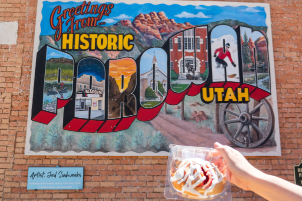 Colorful Greetings from Historic Parowan Utah mural on brick wall with scenic illustrations and pastry in foreground