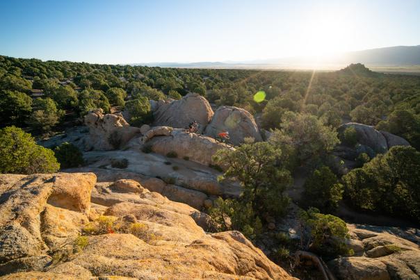 Two people mountain bike across rolling rock formations and high-desert spruce in Three Peaks Recreation Area