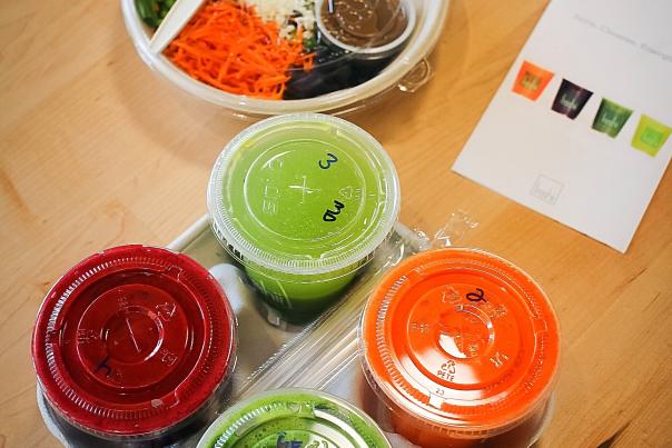 Four multi-colored drinks in a to-go tray and a to-go salad