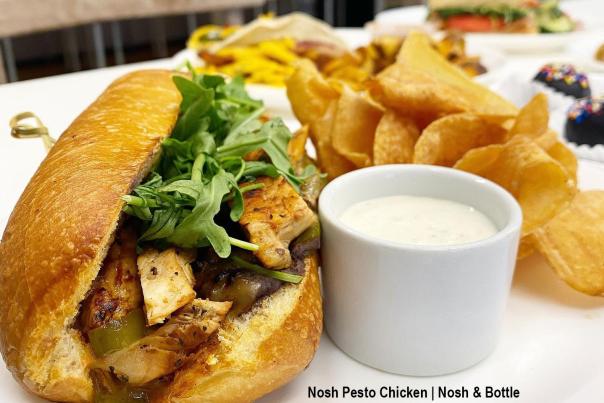 A Pesto Chicken Sandwich from Nosh & Bottle in Irving is served with fresh kettle chips and sauce.