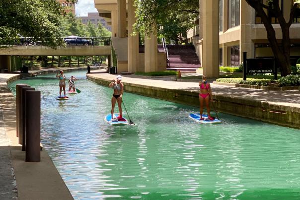 A group winds their way through central Irving via the Mandalay Canal on paddle boards.