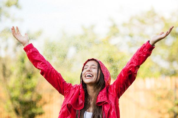 Girl standing in the rain with a red rain coat and arms in the air