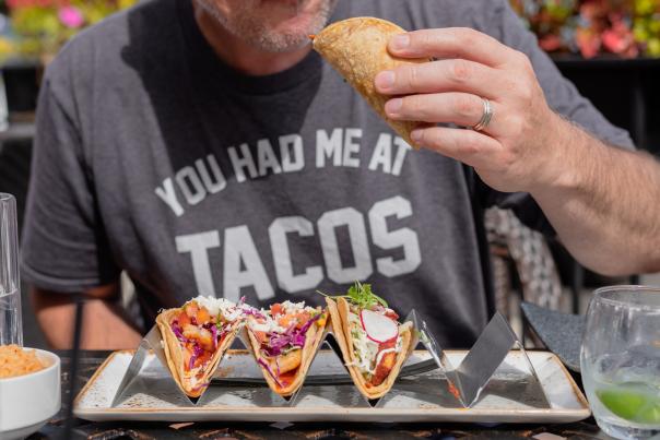 A man enjoys fresh tacos while wearing a t-shirt that reads "You Had Me At Tacos."
