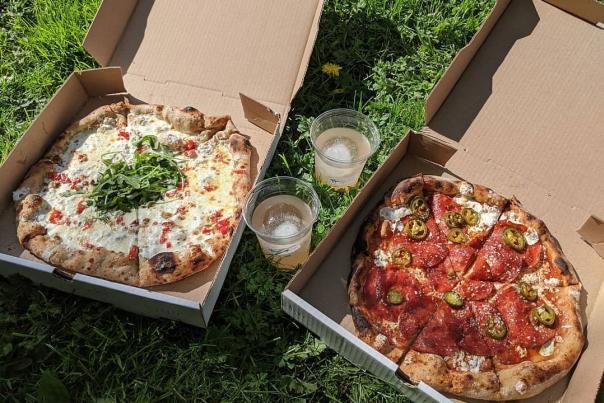 Two takeout pizza boxes side by side with drinks in the middle