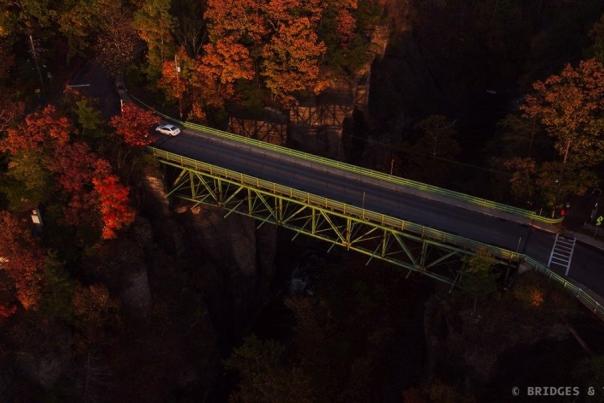 small white car driving over the Stewart Ave bridge. Surrounded by bright red trees in peak foliage.