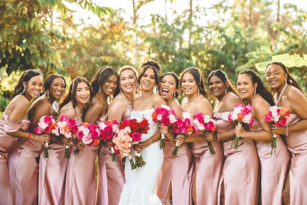 A bride poses with her bridesmaids dressed in pink silk dresses with coordinated hairstyles and tropical pink bouquets in Jamaica