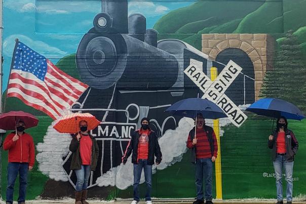 Group Members Stand Holding Umbrellas in Front of New Railroad Mural