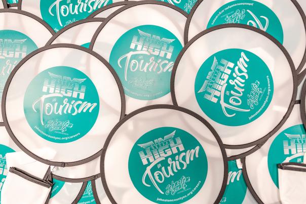 Teal frisbees that say "Aim High in Tourism" are spread out across a table top.