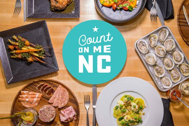 Bright blue Count On Me NC badge icon on a photo of plates of food laid out on a wooden table top.