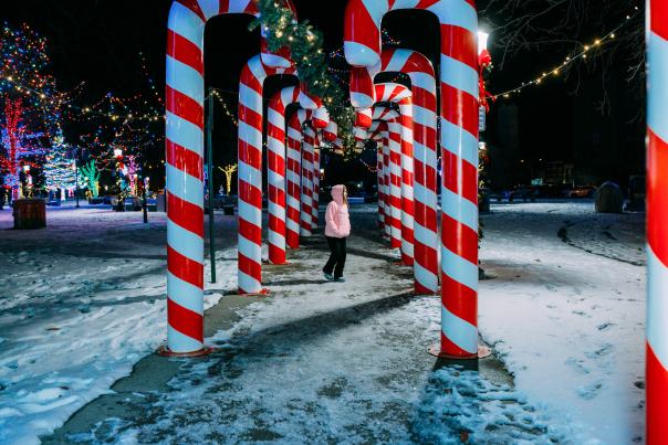 A woman stands in between tall, lighted candy canes in Cany Cane Lane at Bronson Park.