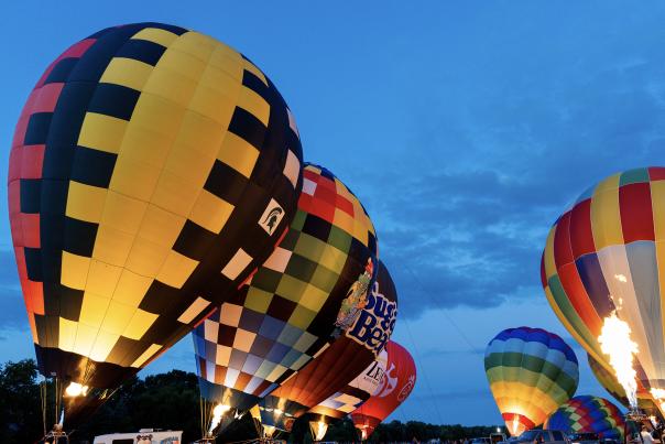 A variety of hot air balloons rest in a field at dusk during Gull Meadow Farms' Kalamazoo Balloon Festival.