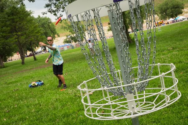 disc golf basket with a man in the background throwing a disc