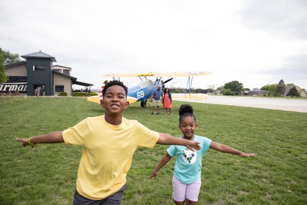 Kids joyfully running through a grassy field with a biplane in the background