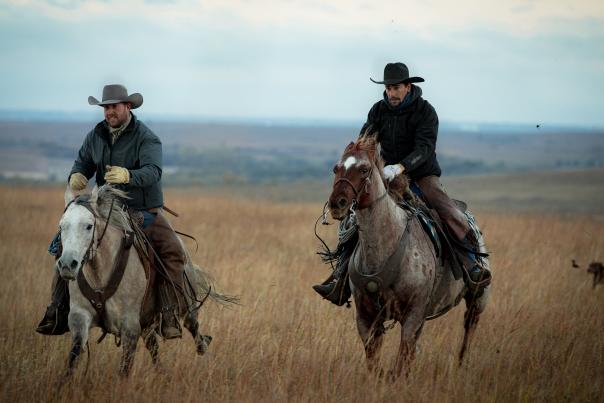 Two cowboys ride through a field