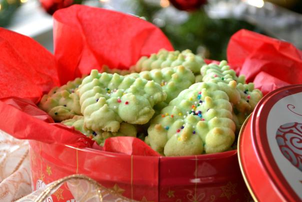 green holiday cookies with sprinkles inside a holiday tin and red tissue paper