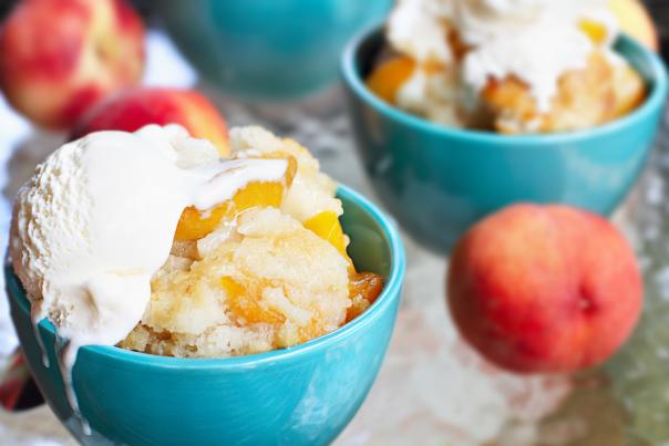 a group of teal color bowls filled with peach cobbler topped with vanilla ice cream.