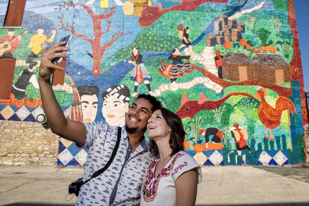 Man and woman taking selfie in front of a Hmong mural in downtown Kansas City, KS