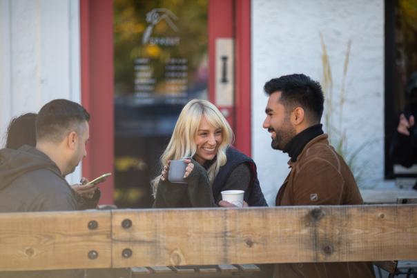Friends_Sitting_Outdoors_Laughing_and_Holding_Hot_Drinks