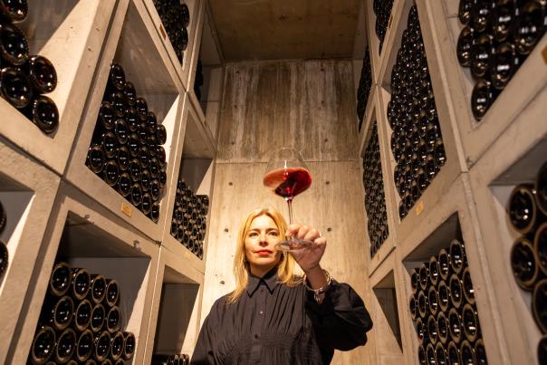Woman_Holding_Up_a_Glass_of_Red_Wine_Inside_the_Wine_Library_Surrounded_by_Bottle_Filled_Shelves