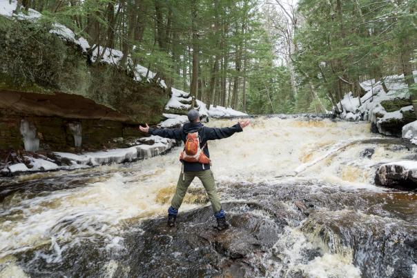 Man stands in center of waterfall during winter with arms open.
