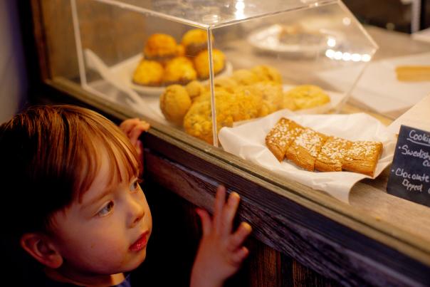 a child looks longingly into a bakery case filled with goodies