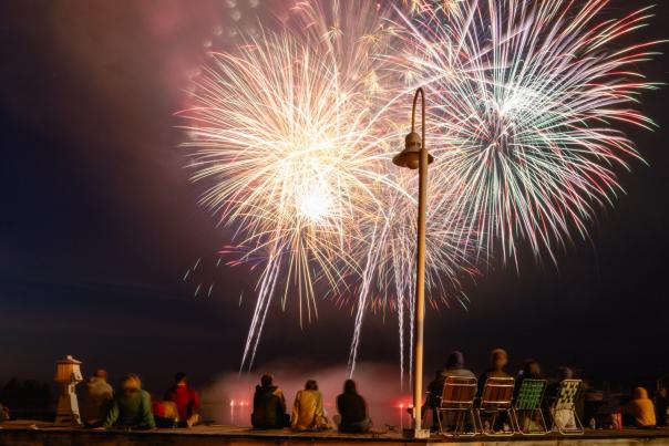Group of people sit on dock watching fireworks.