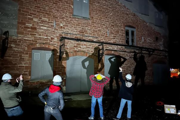 people in hardhats play with shadows against a brick building