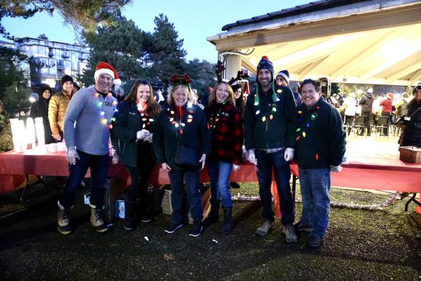 Group of 6 festively dressed people in front of red tables in Marina Park in Kirkland, WA.
